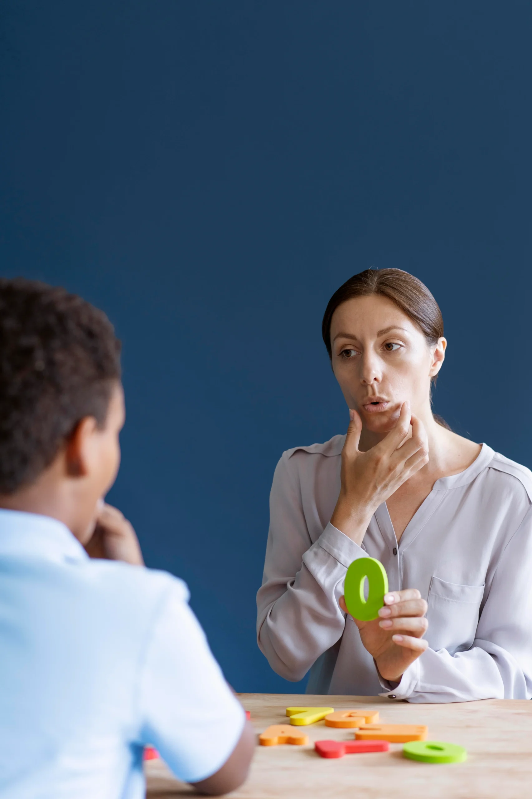 A behavioral therapist guiding a young boy through a therapy session using visual aids and facial modeling techniques.