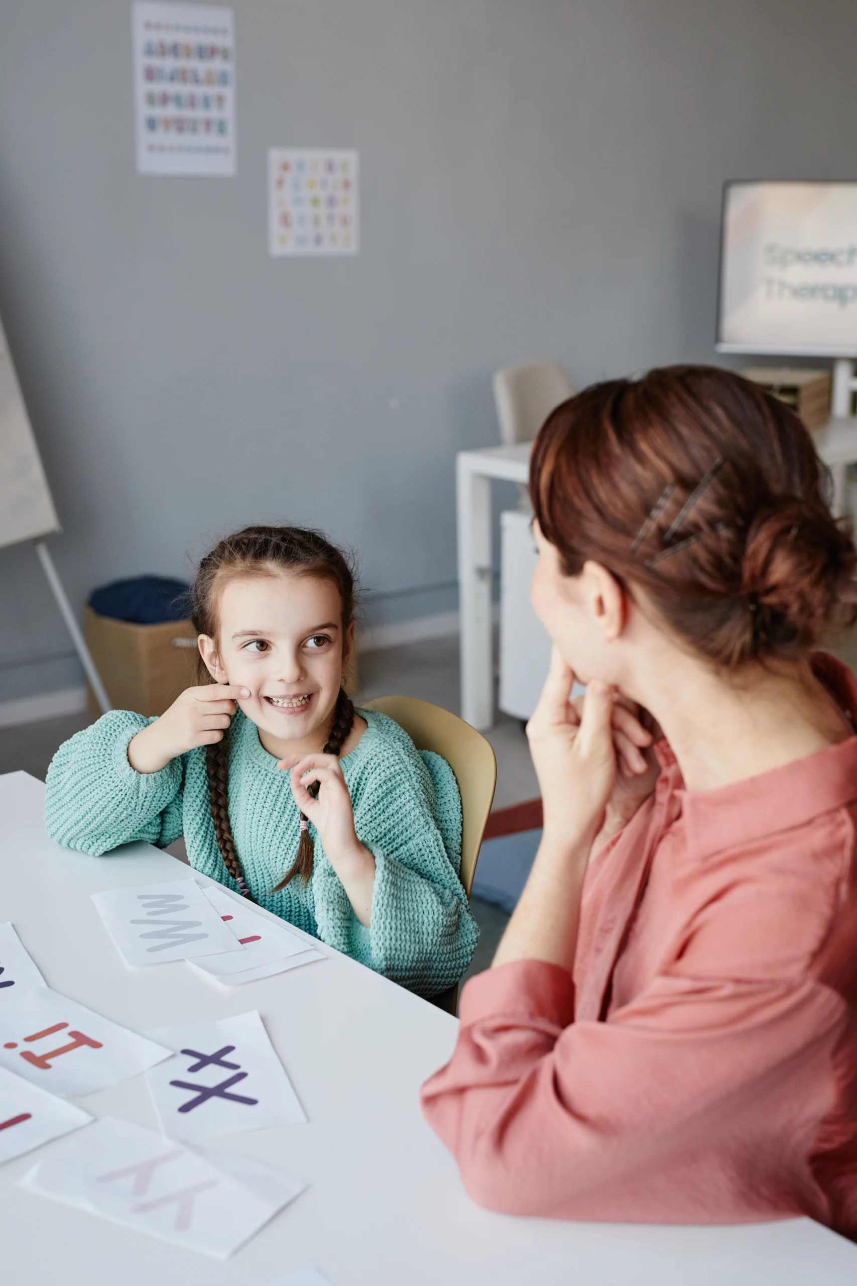 little-girl-doing-articulated-exercises-together-with-her-teacher-table-classroom Child and therapist practicing speech therapy in Kerala classroom.