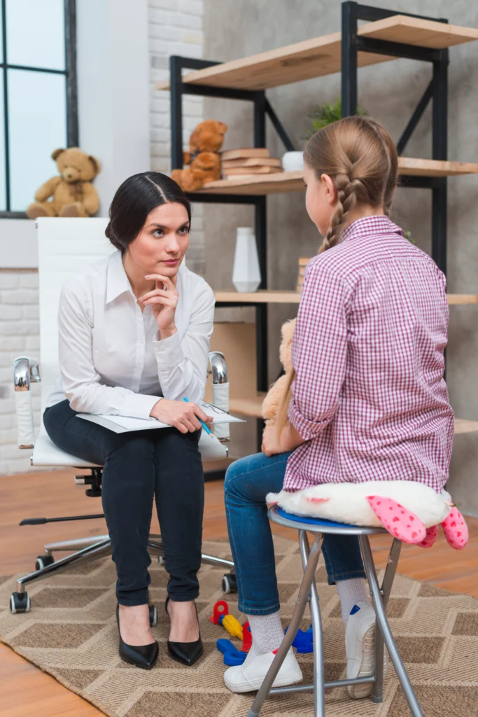 Child psychologist attentively listening to a young girl during a behavioral therapy session in a calm, supportive environment.