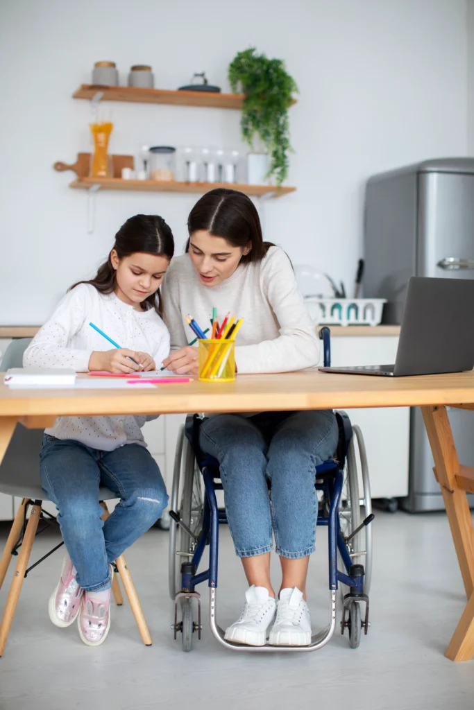 Young girl and her mother in a wheelchair working together on a drawing at home, promoting inclusion and support in special education services.