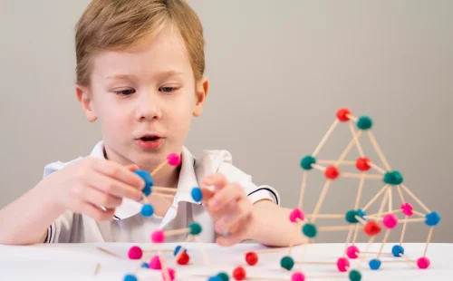 boy-playing-with-colorful-atoms-game-home A young boy engages in a hands-on activity, building 3D structures with colorful balls and sticks, promoting creativity and problem-solving