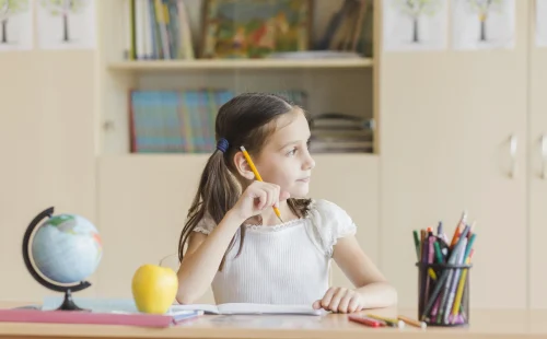 learning space Child sitting at a classroom desk thinking while holding a pencil, surrounded by school supplies and a globe.